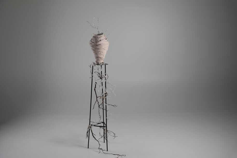 Tall metal stand holds a beige vase wrapped in twine, with bare tangled branches trailing down