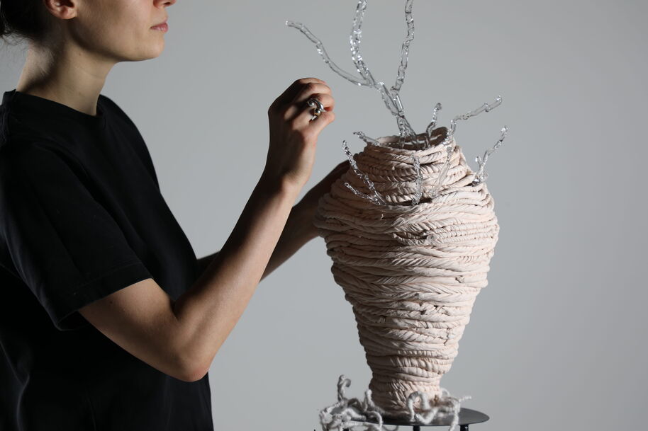 Person in black shirt shaping a beige twisted sculpture with clear branch-like rods on top