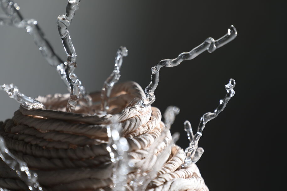 Close-up of a coiled beige rope basket with clear glass-like tendrils against a dark background