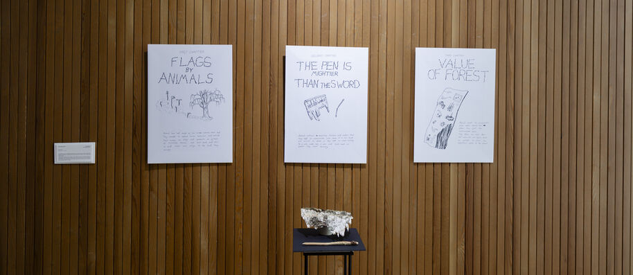 Three white illustrated posters on a tall wooden wall above a small dark stand with a pale sculpture.