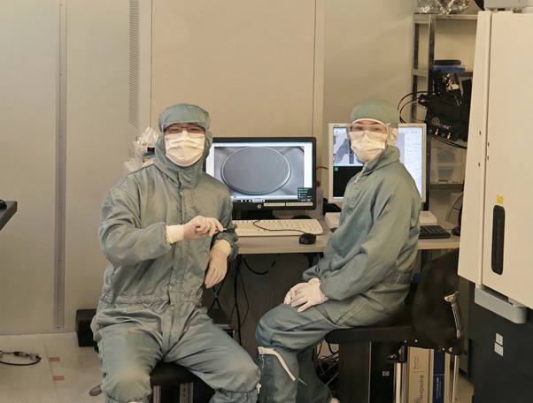 Kaksi henkilöä puhdastilapuvuissa laboratorioissa, tarkastelevat näytöllä näkyvää pyöreää näytettä