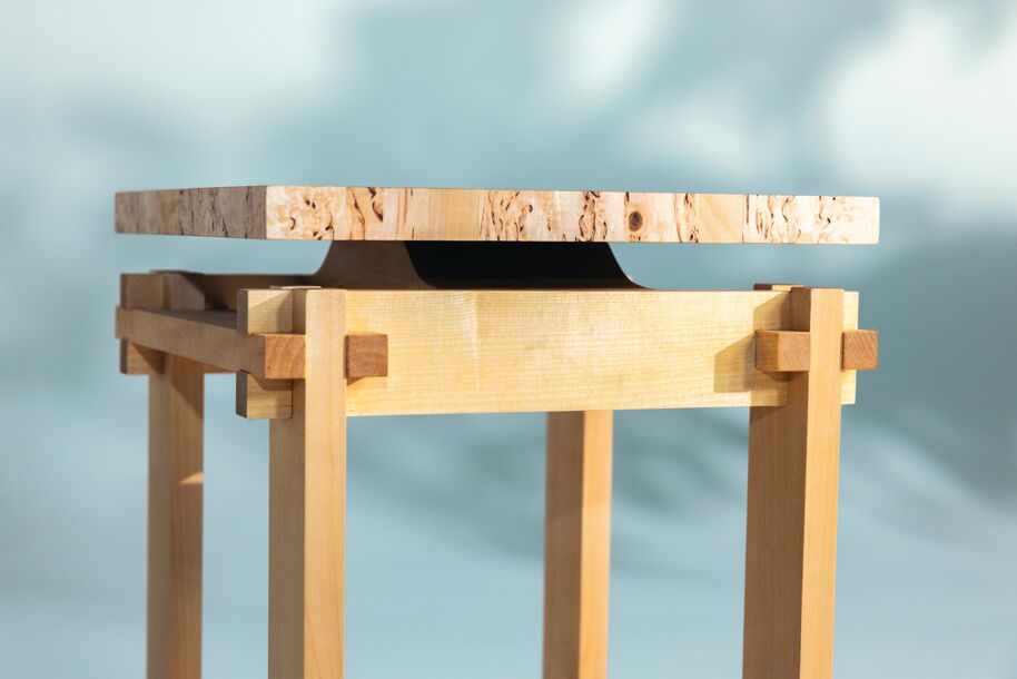 Close-up of a light wooden side table with a thick, patterned top and simple joined legs