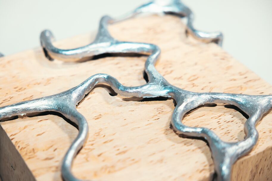 Curving silver metal in organic shapes set into a pale textured wooden block