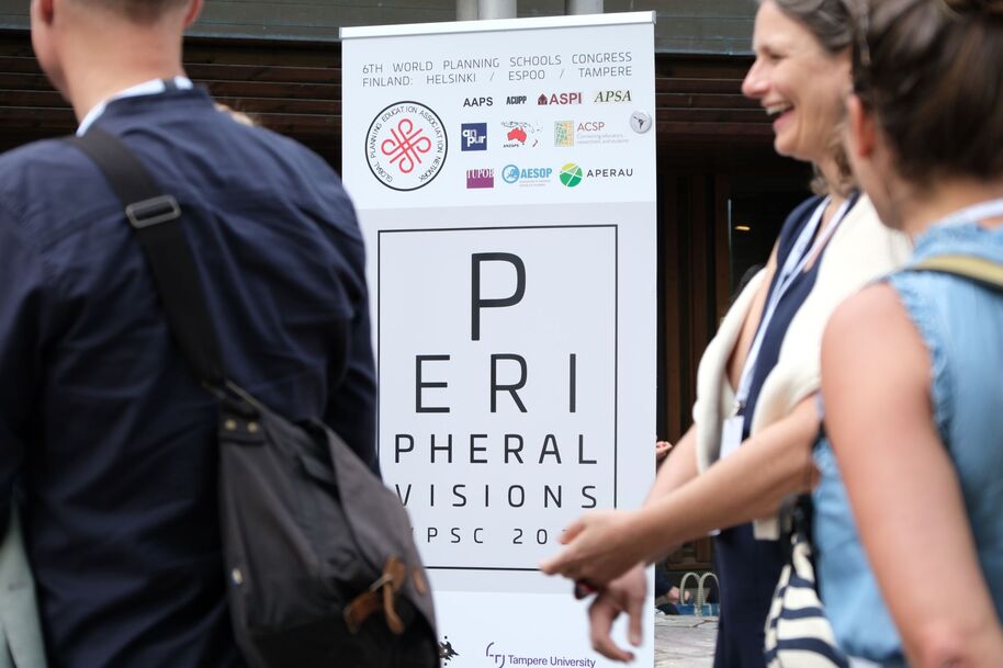 People at a WPSC congress standing near a tall white PERIPHERAL VISIONS banner