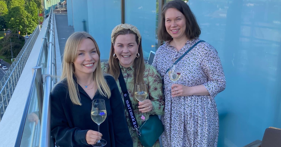 The Kenno team, formed by three women, smiling at the camera with glasses in their hands standing up