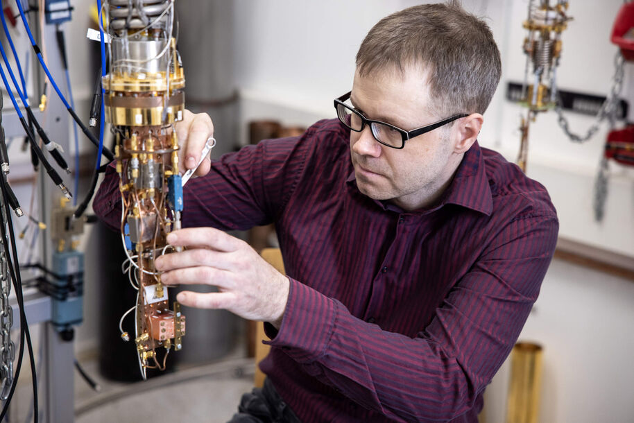 Man in glasses adjusts a tall gold-coloured scientific device with cables in a lab