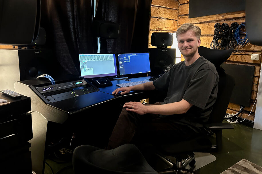 Sauli Norja sits in a dark studio at mixing desk with dual monitors, speakers and wooden walls behind