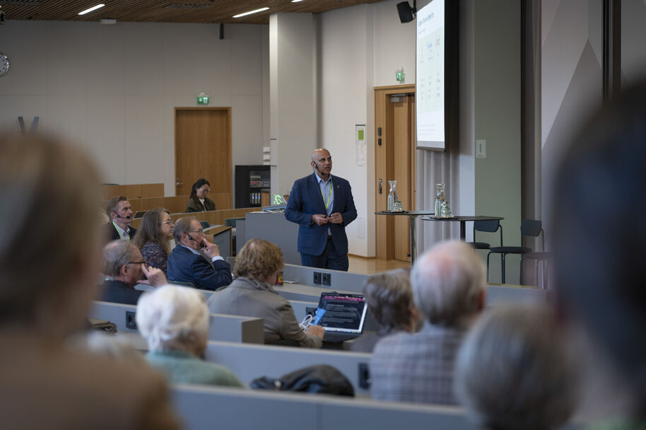 Sinitakkinen Munir Mandviwalla esitelmöi istuvalle yleisölle modernissa luentosalissa