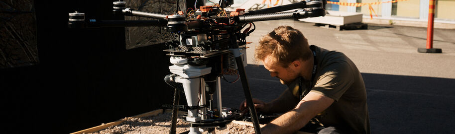 A male student is hunching over a drone device in a parking lot.