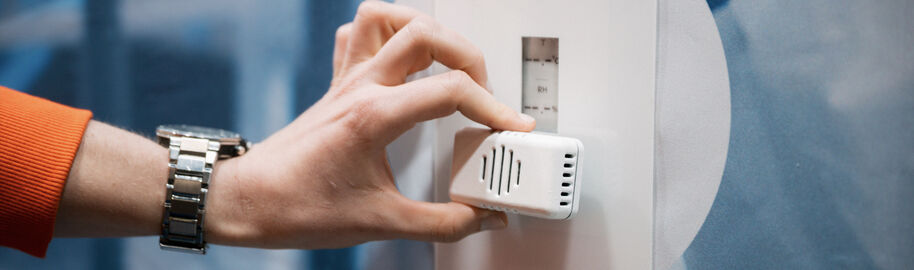 A hand is holding a small device in from of an interface on a wall.