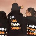 Three people wearing black hoodies with various designs of '5000€' printed on the back.