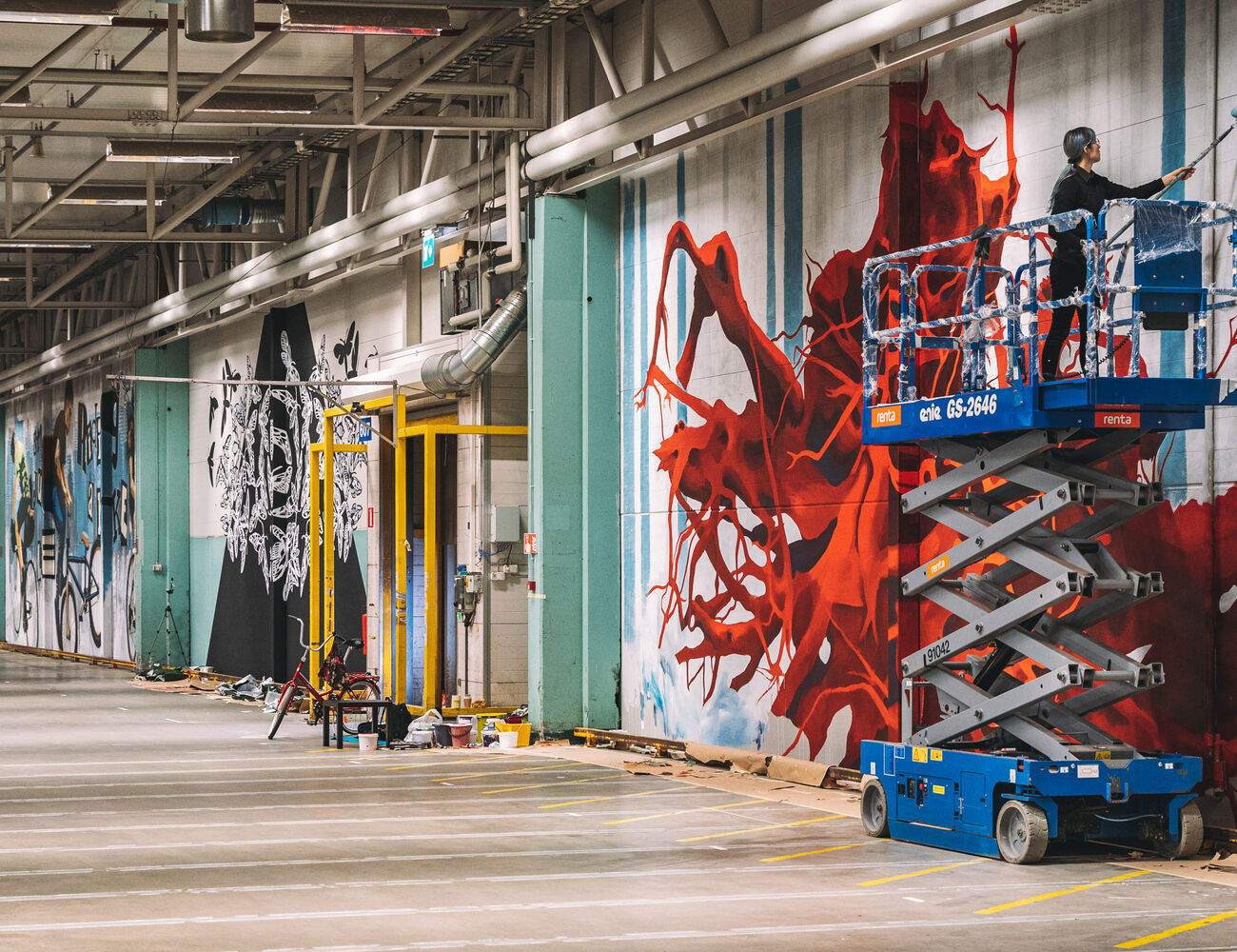Image of Concreate artists installing their work in Keran Hallit. Artist Saara Salmi stands on a scissor-lift to reach her painting