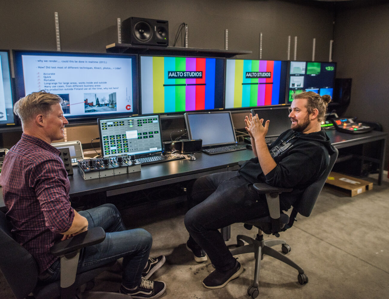 Two people sit facing each other by a large editing table, intensily interacting with each other