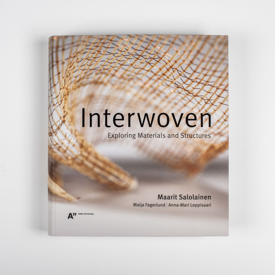 Interwoven-kirjan harmaansävyinen kansi, jossa on kuparilankainen kudos.
