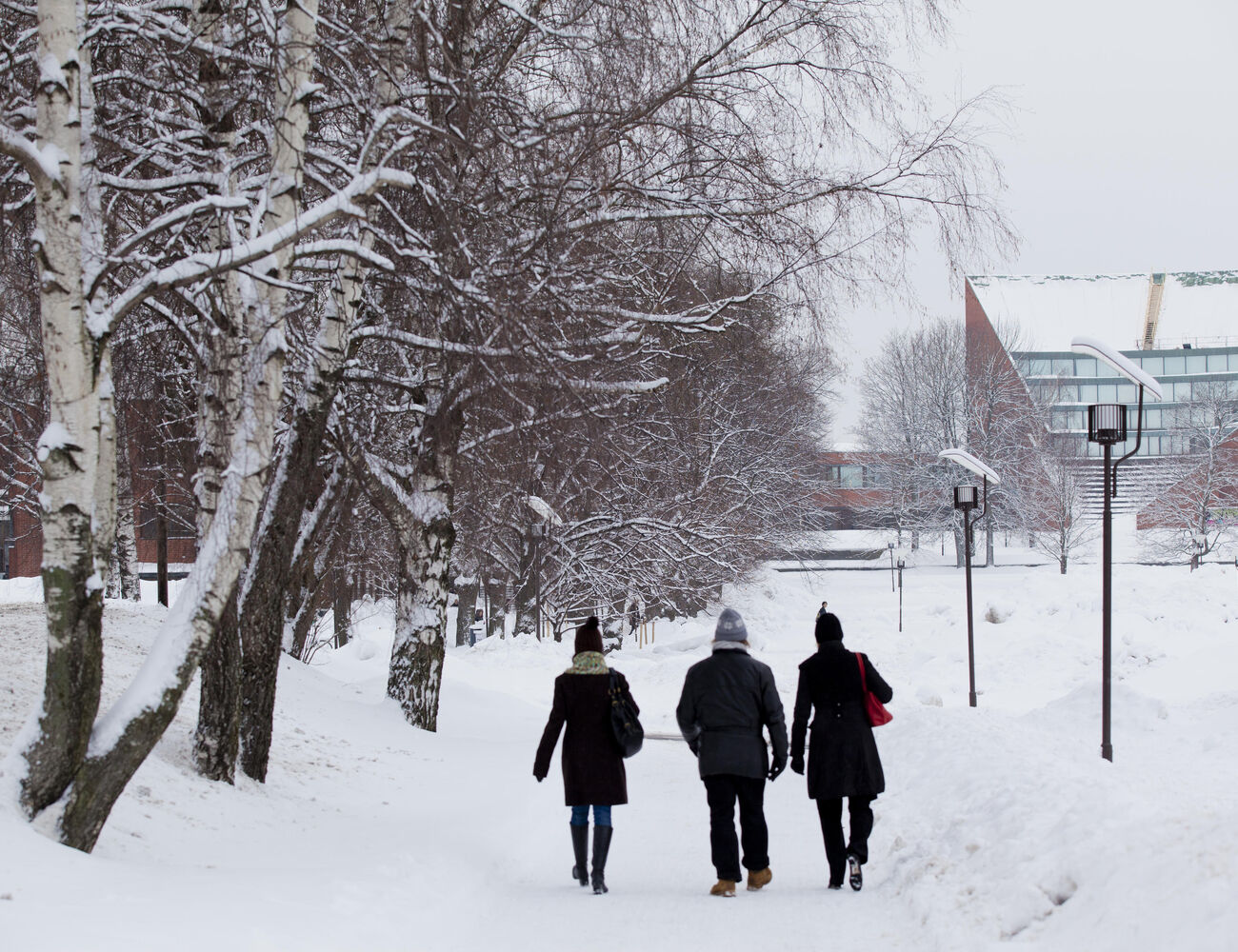 Three people walking on Otaniemi campus on a snowy day. Aalto buildings in the background. Photo: Aalto University / Mikko Raskinen.