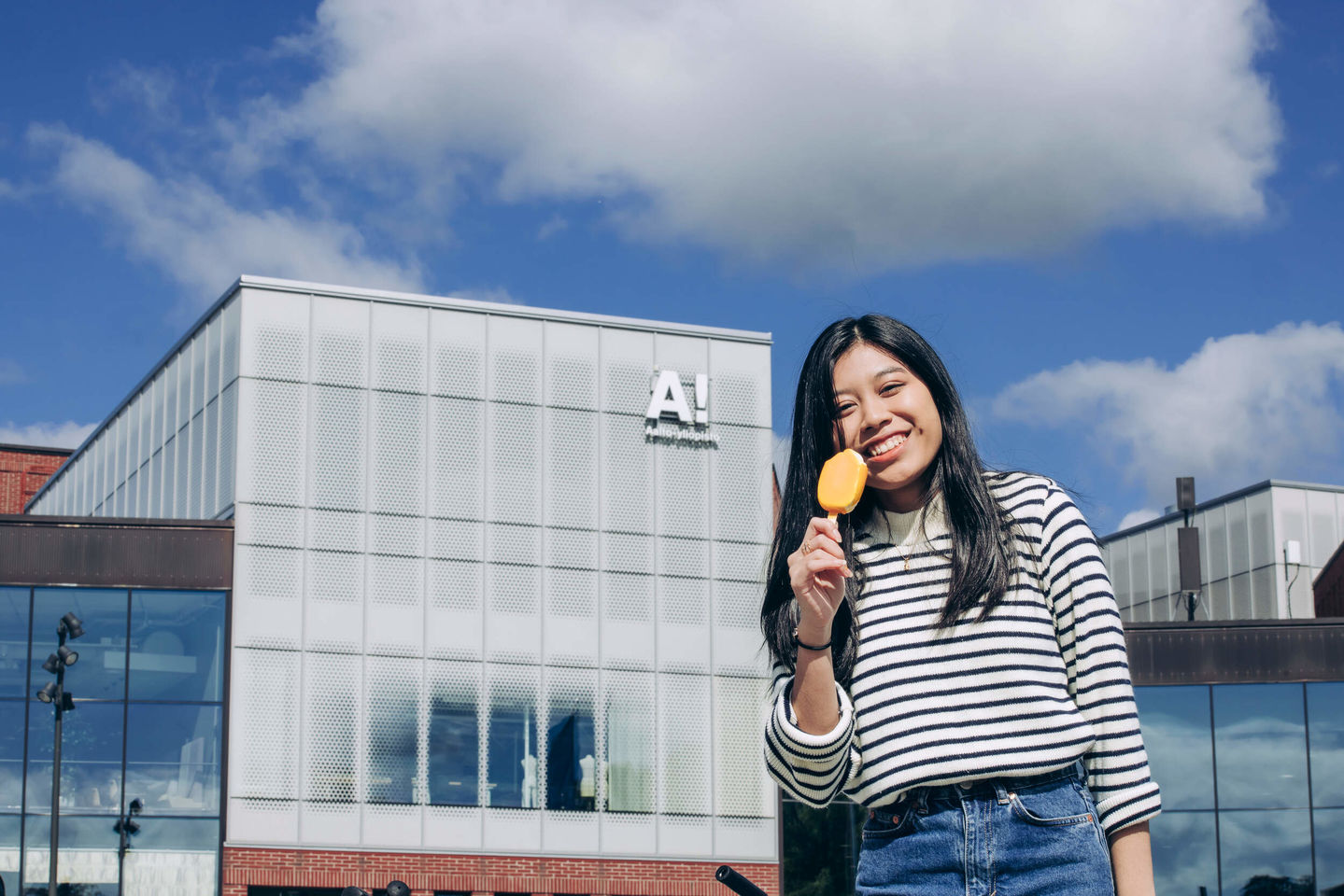 A student eating a yellow ice cream in fron of Aalto University campus.