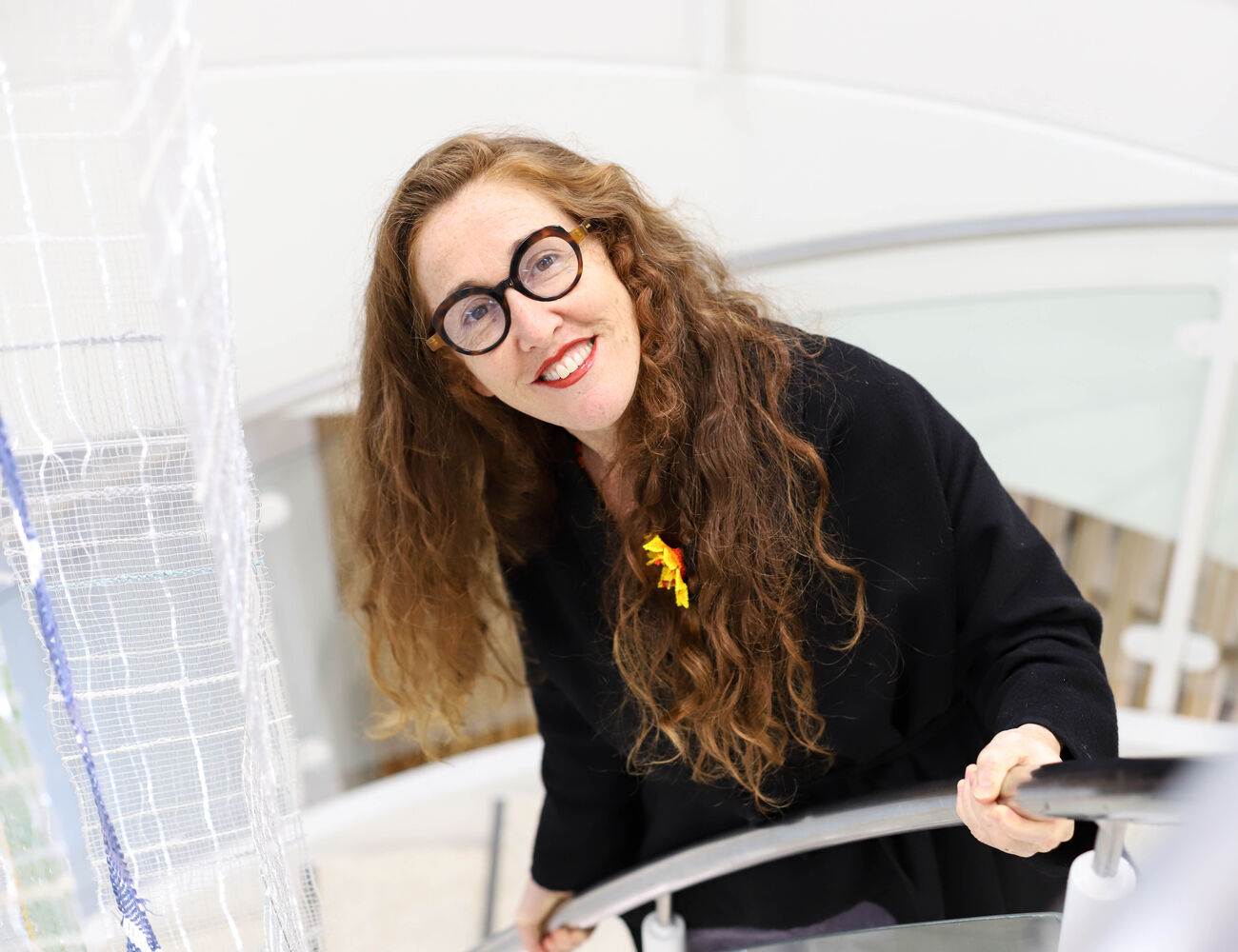Smiling woman with glasses and long hair standing on the staircase and looking up at the camera