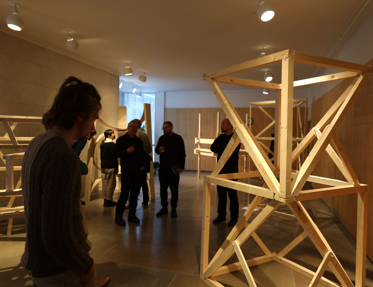People look at wooden frames that are standing in the marble exhibition space