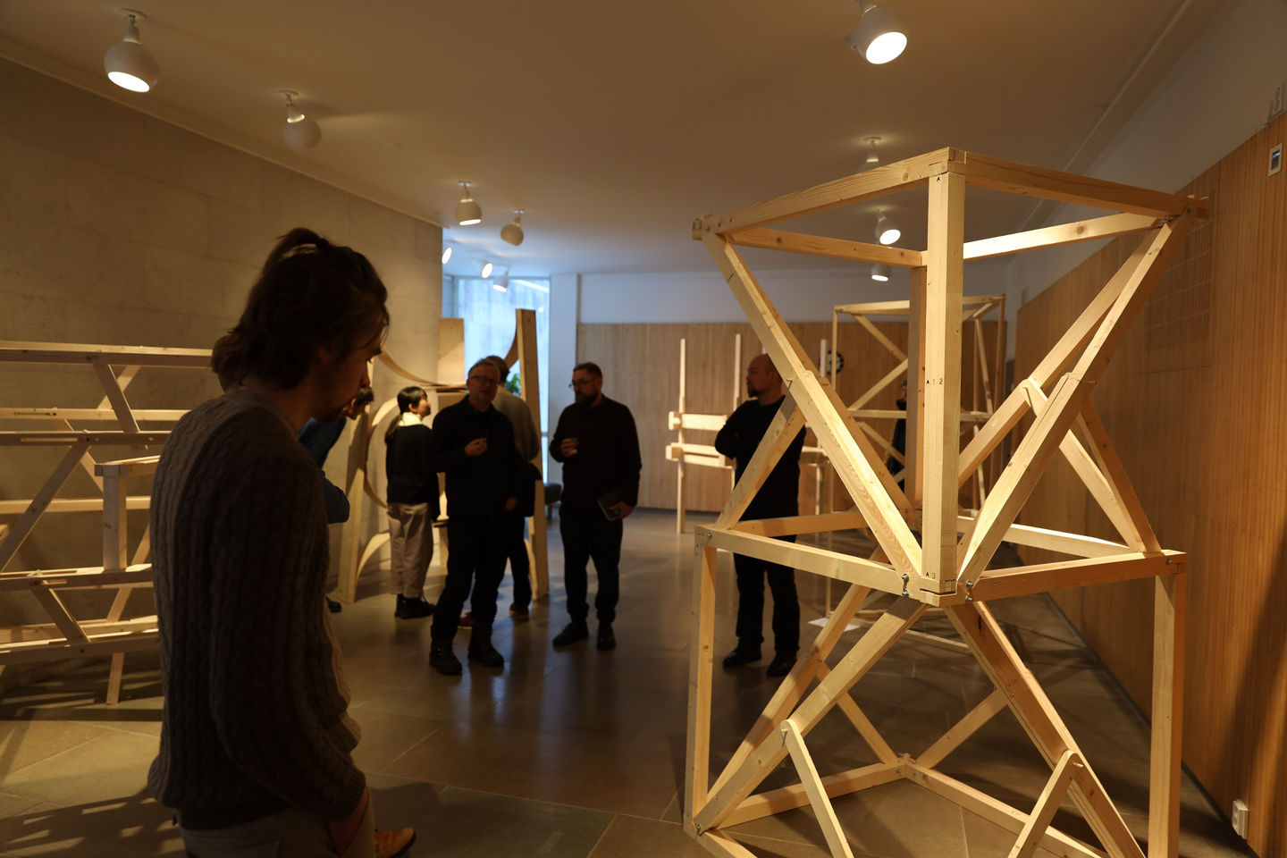 People look at wooden frames that are standing in the marble exhibition space