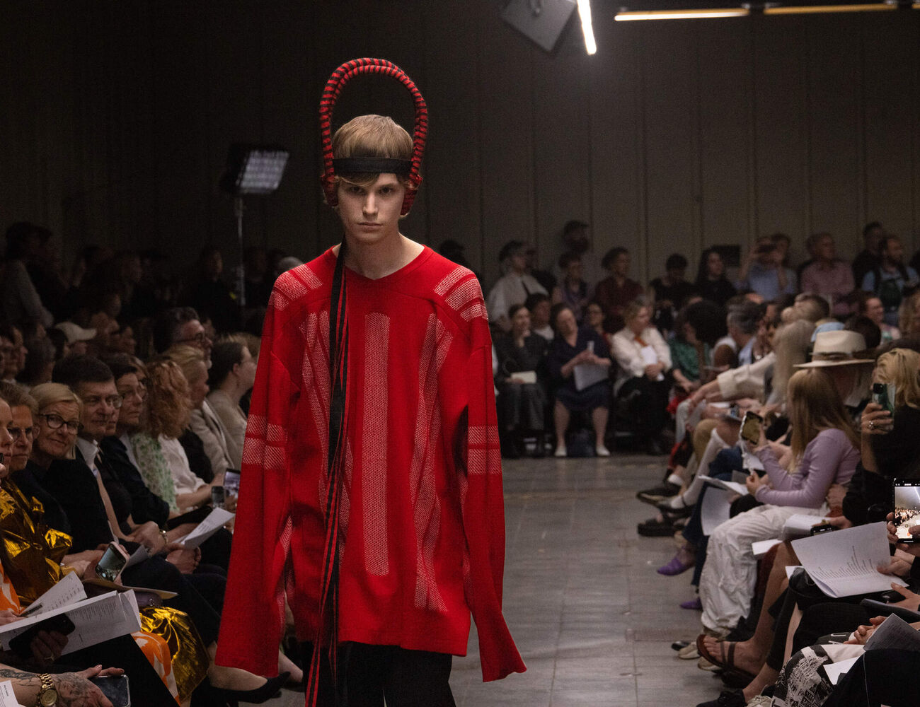 Model walks the catwalk in red outfit and red headpiece