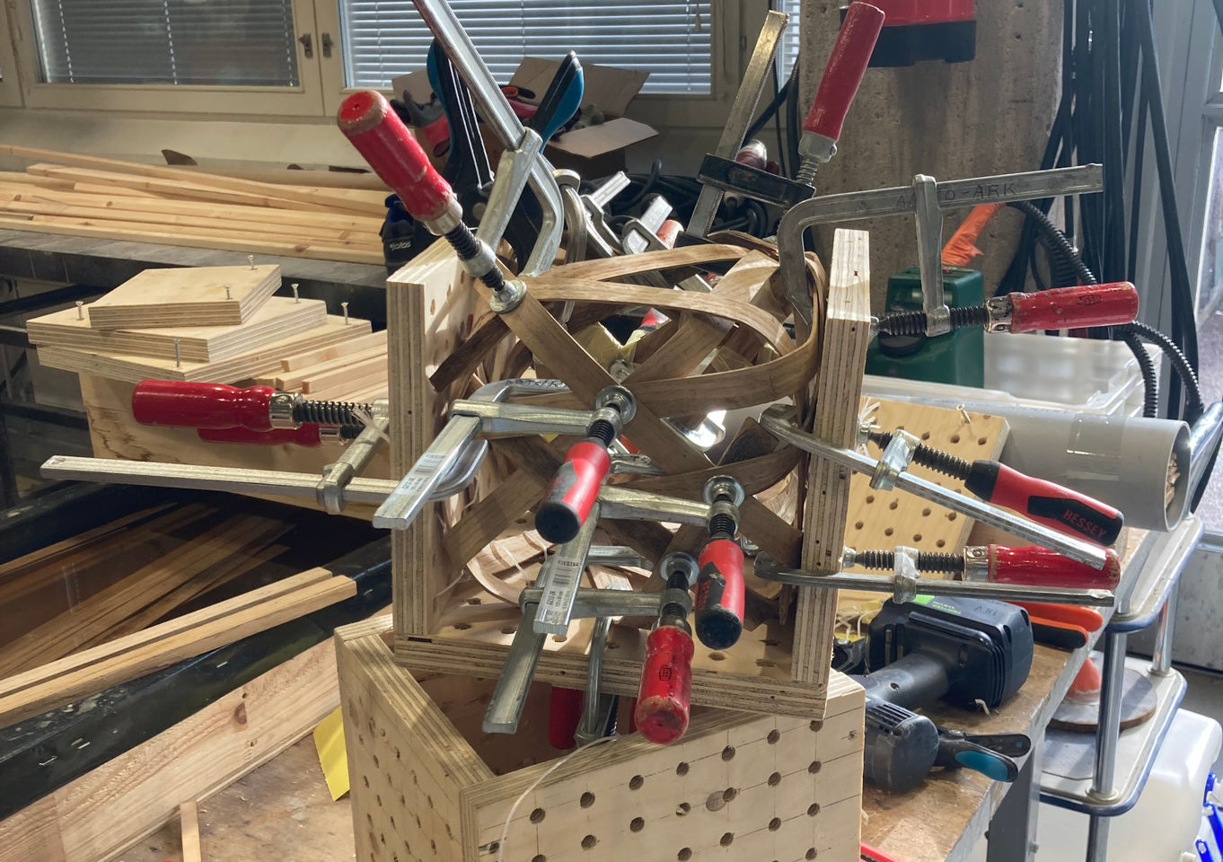 Cube made of bent strips of oak, still in the square plywood mold with big clamps holding it while glue dries