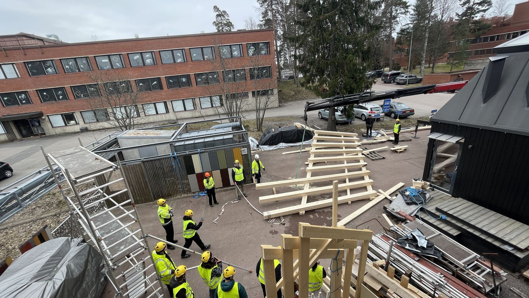 The truss lying on the ground waiting to be lifted, students standing around wearing safety gear