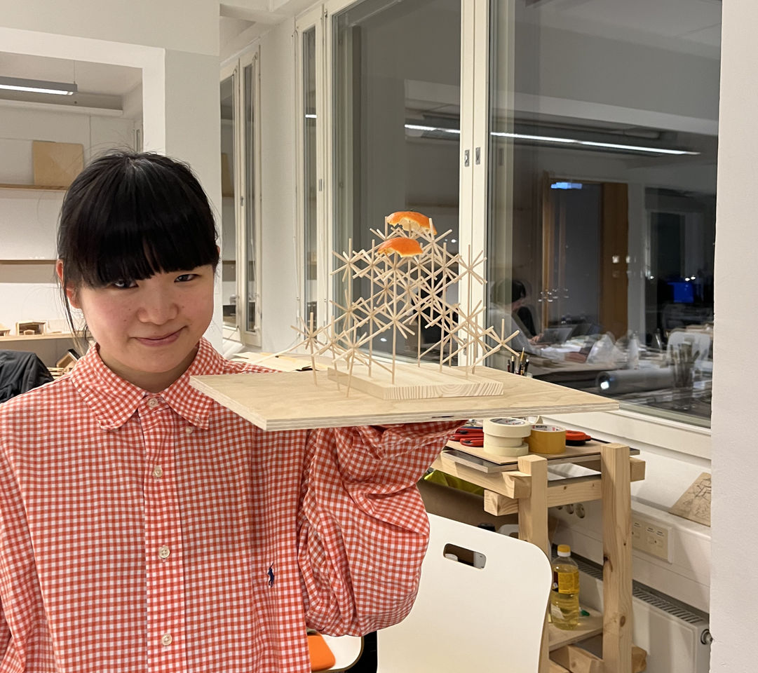 Student Meina holding up a wooden scale model of her design proposal, with two orange peels figuring as improvised roof