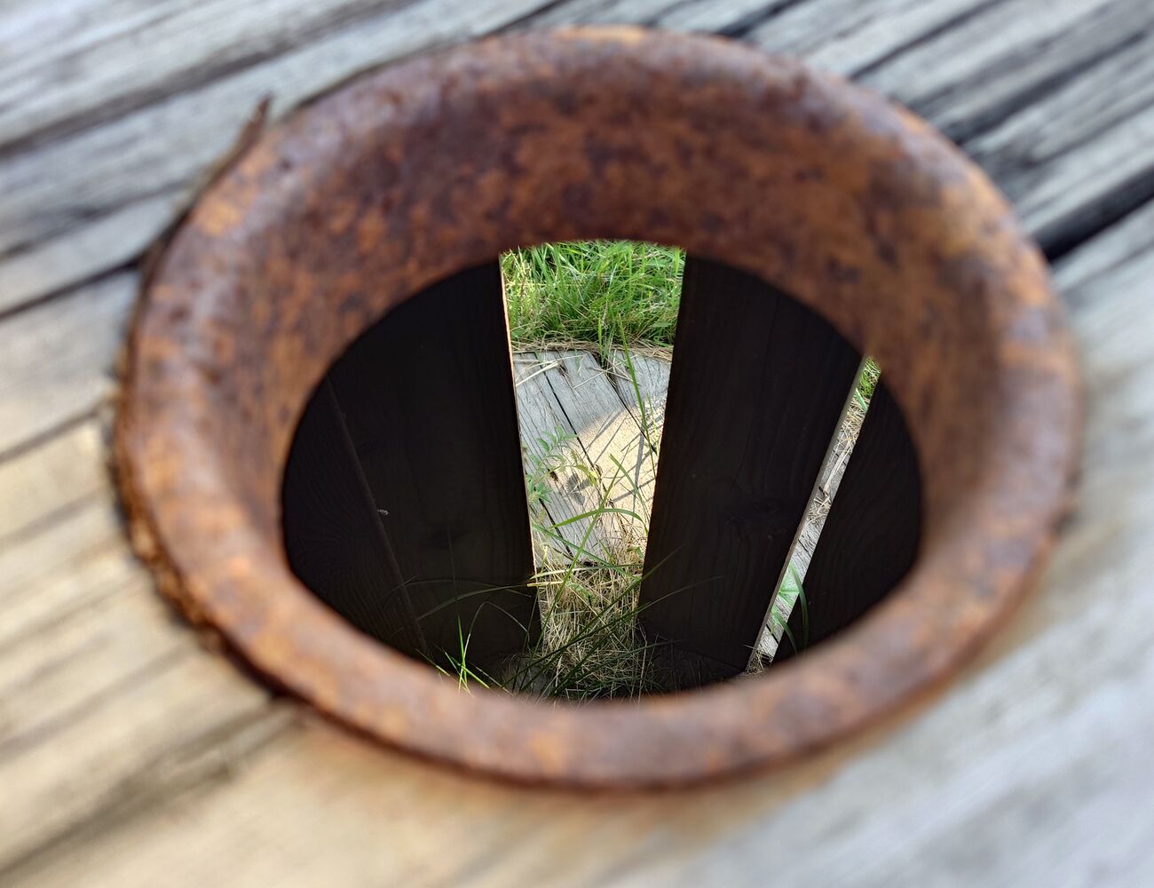 Rusty metal on grey wood, grass can be seen through the hole