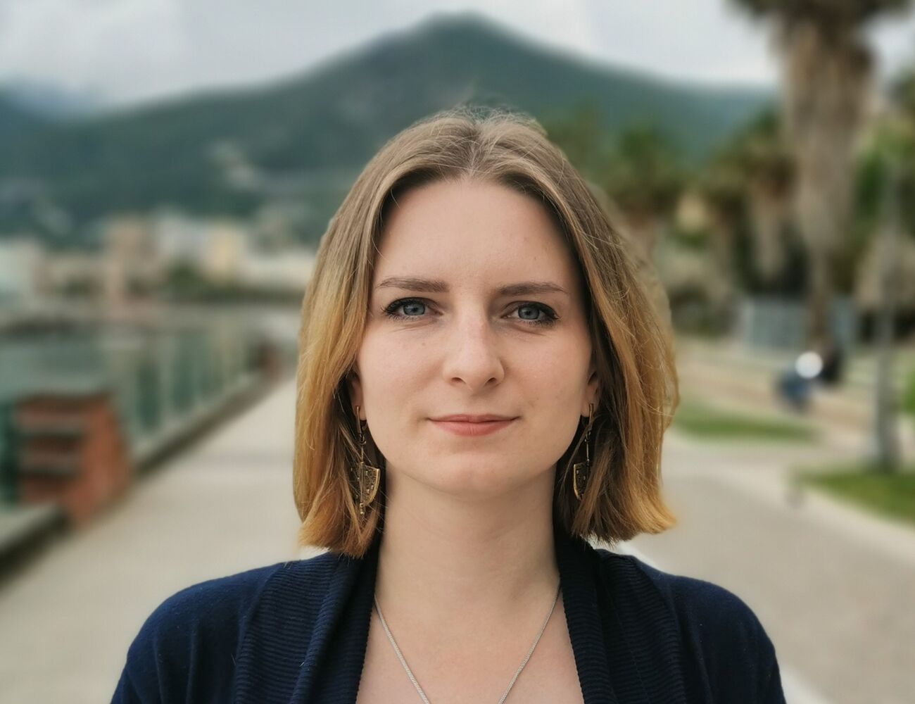 A close-up photo of a person in long bob hair and a mountain landscape in the background.