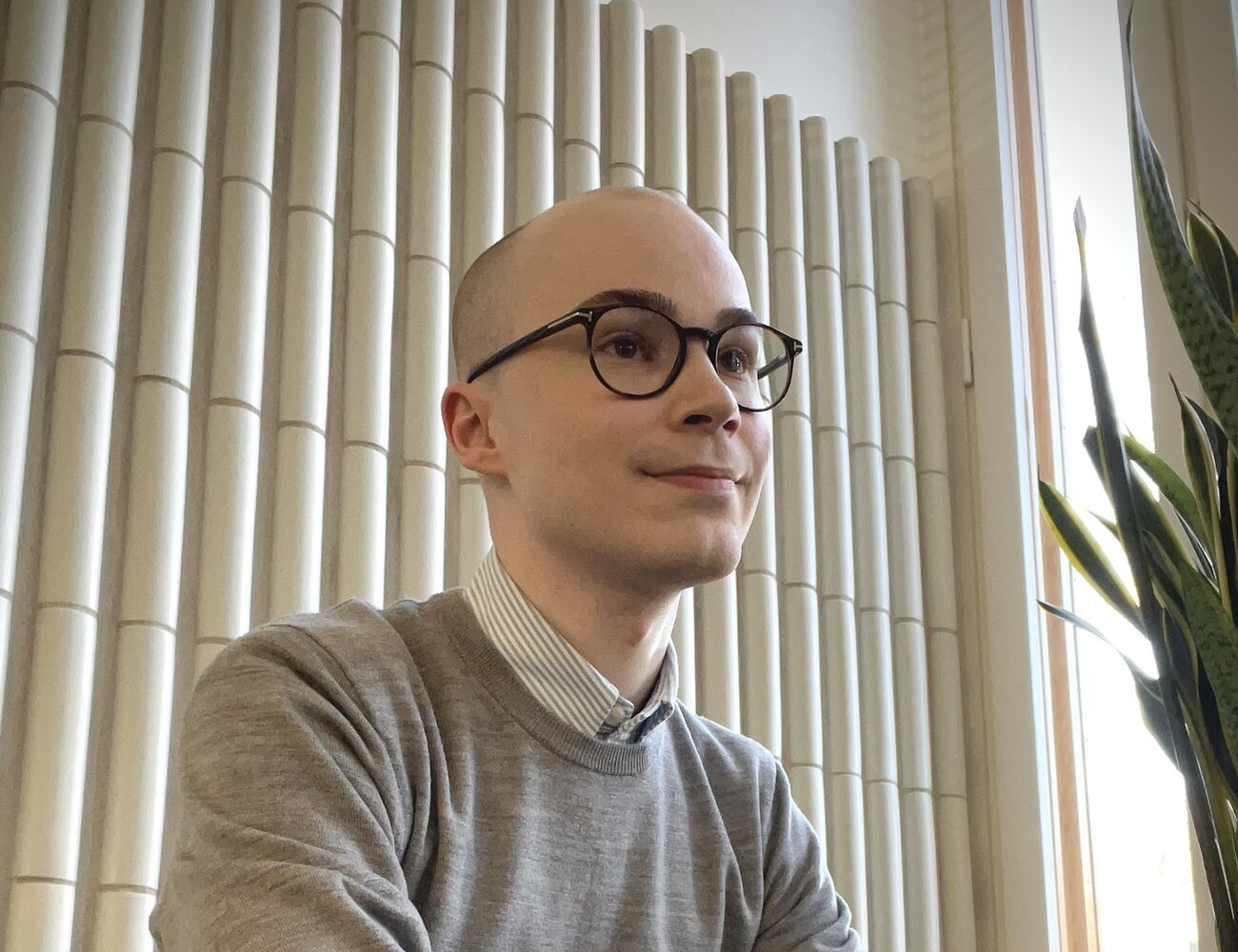 A PhD researcher with dark glasses sits near a window on the Aalto University campus.