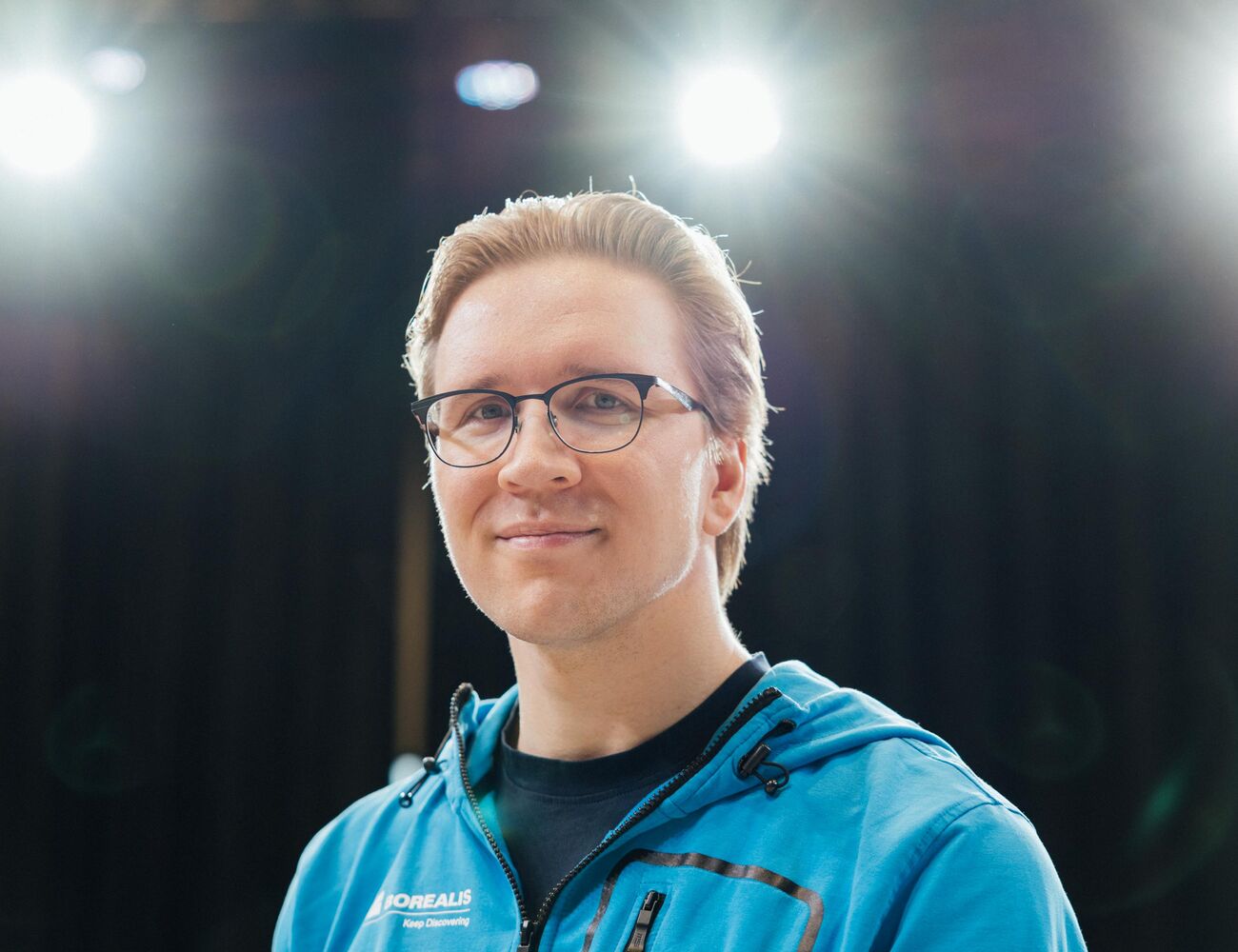 Person wearing a blue jacket under bright stage lights, with a black background.