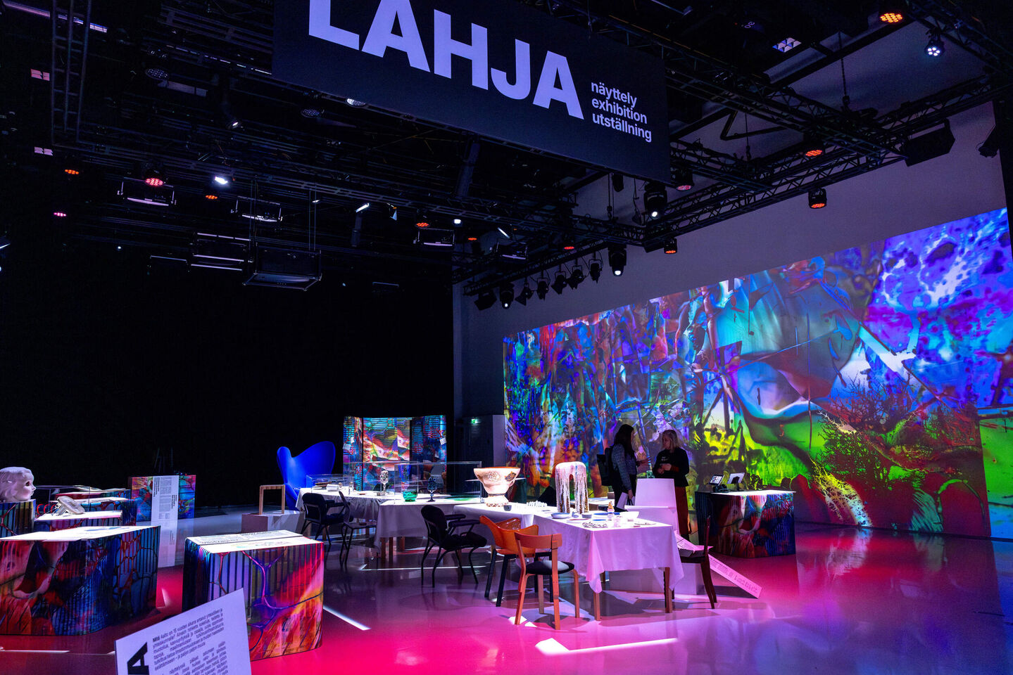 Modern exhibition room with colourful abstract projections on the walls and various artworks on display.