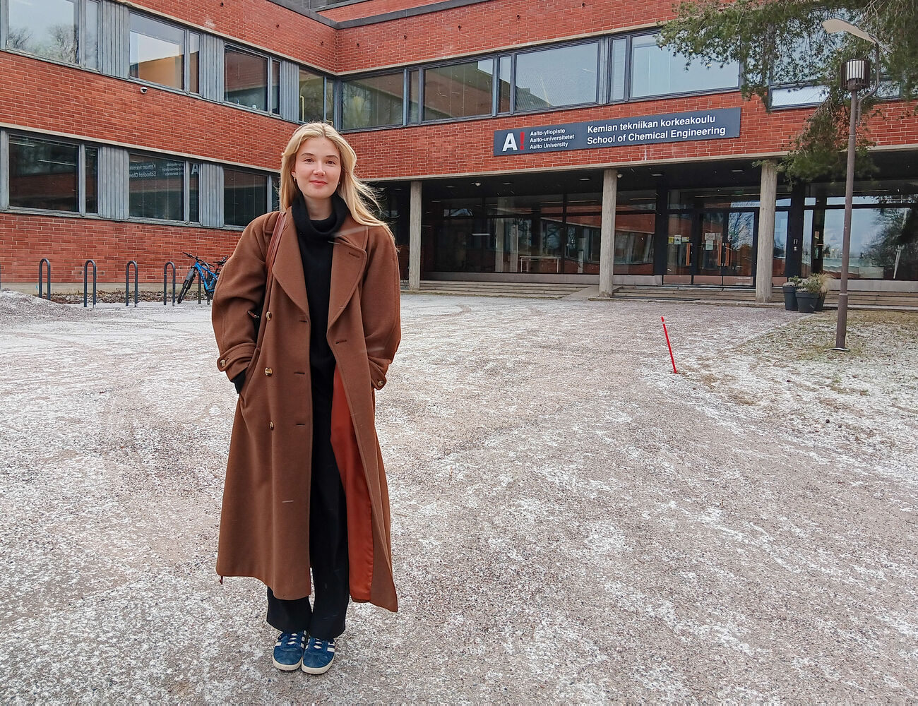 En person i en lång brun kappa står framför en byggnad med skylten 'School of Chemical Engineering'.
