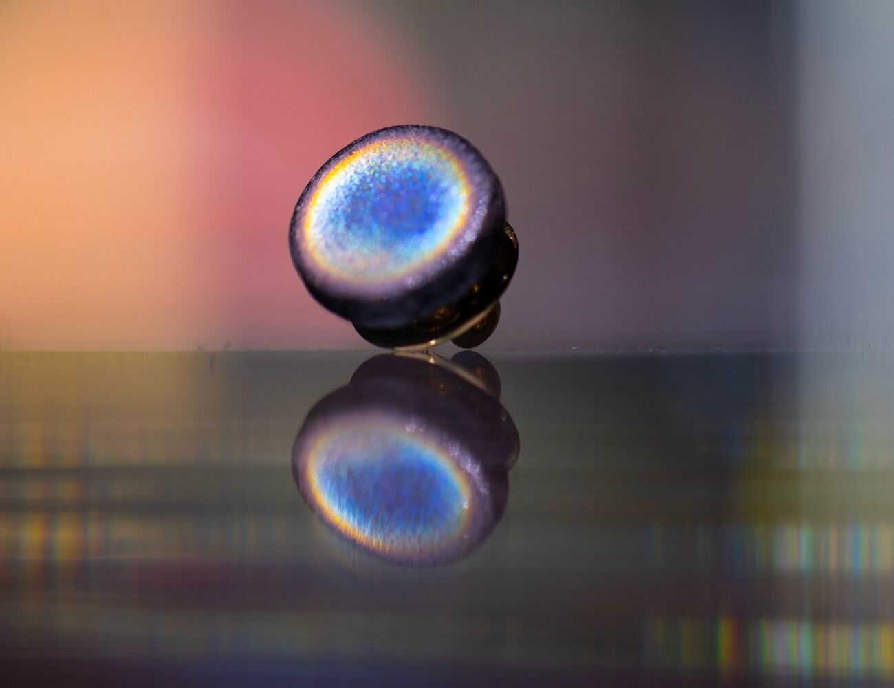 Close-up of a iridescent, round campaign pin reflecting on a shiny surface with a blurred colourful background.