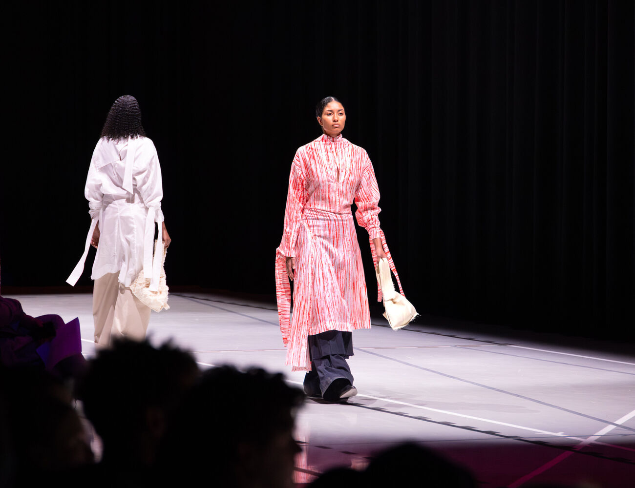 Three models on a runway, one in a red and white dress, another in white and third in beige and black outfit.