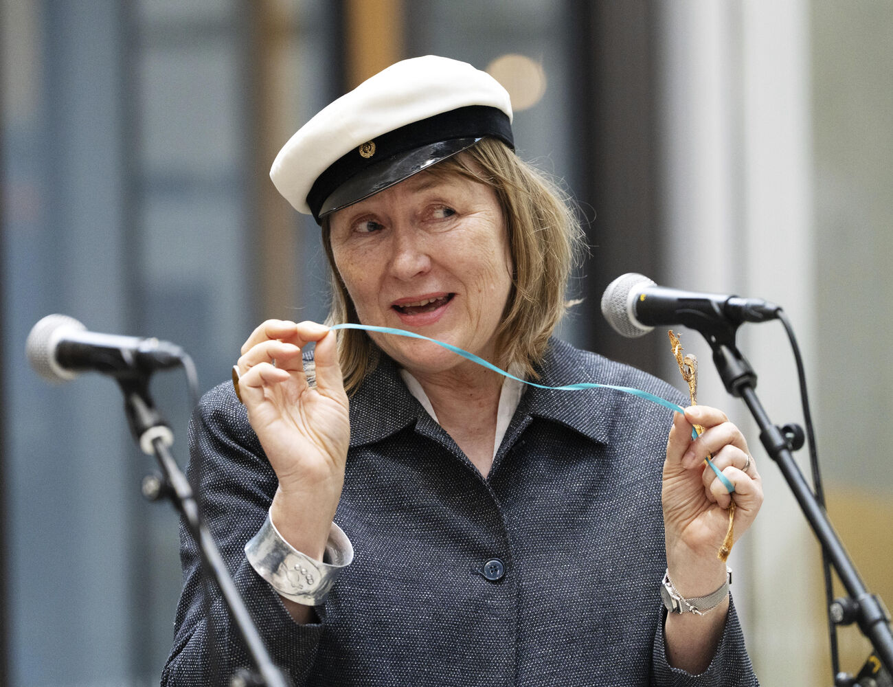 A person wearing a grey coat and white hat speaks into a microphone while holding a thin string.