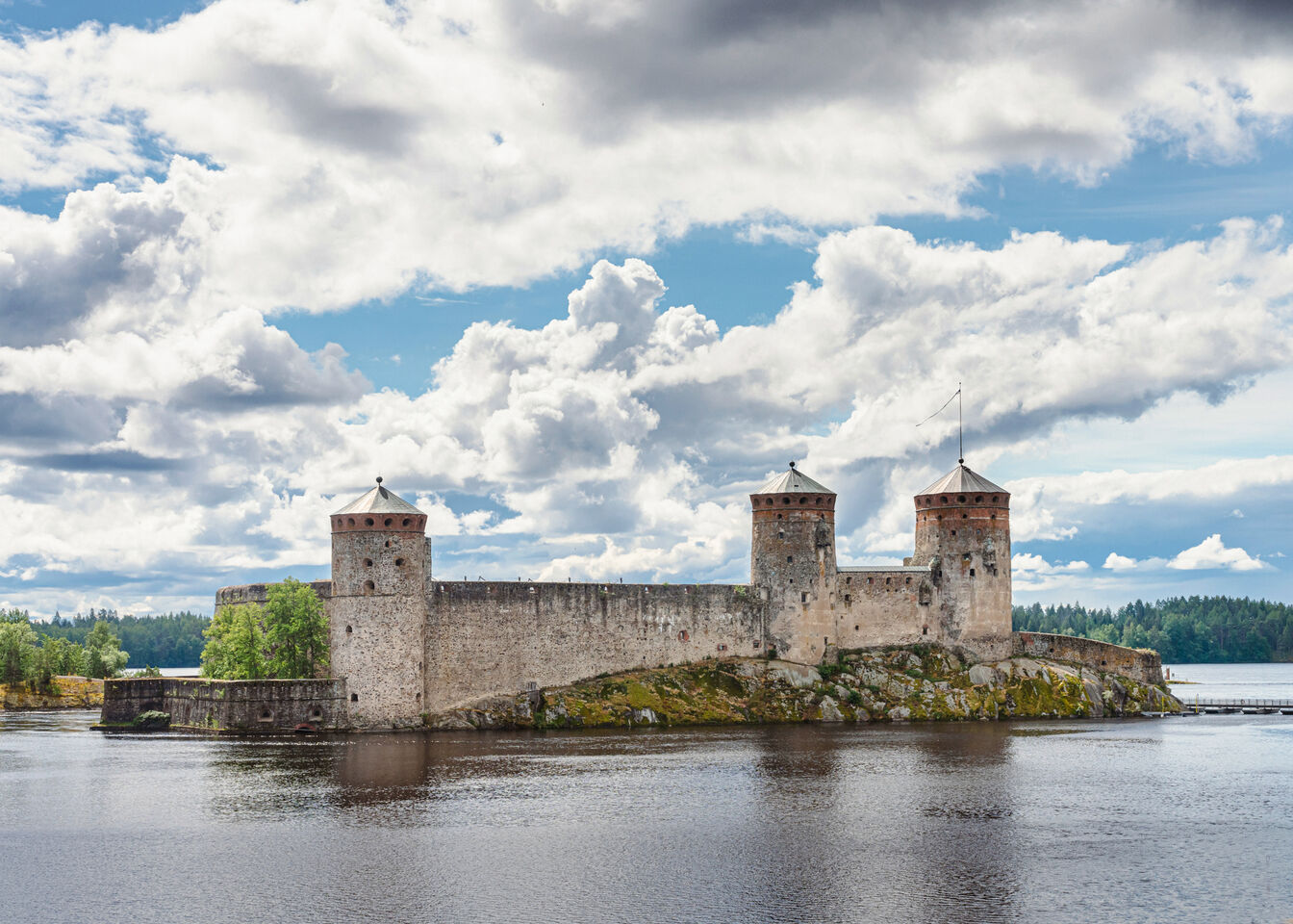 Keskiaikainen linna, jossa on kolme kivitornia saarella veden ympäröimänä, osittain pilvinen taivas.
