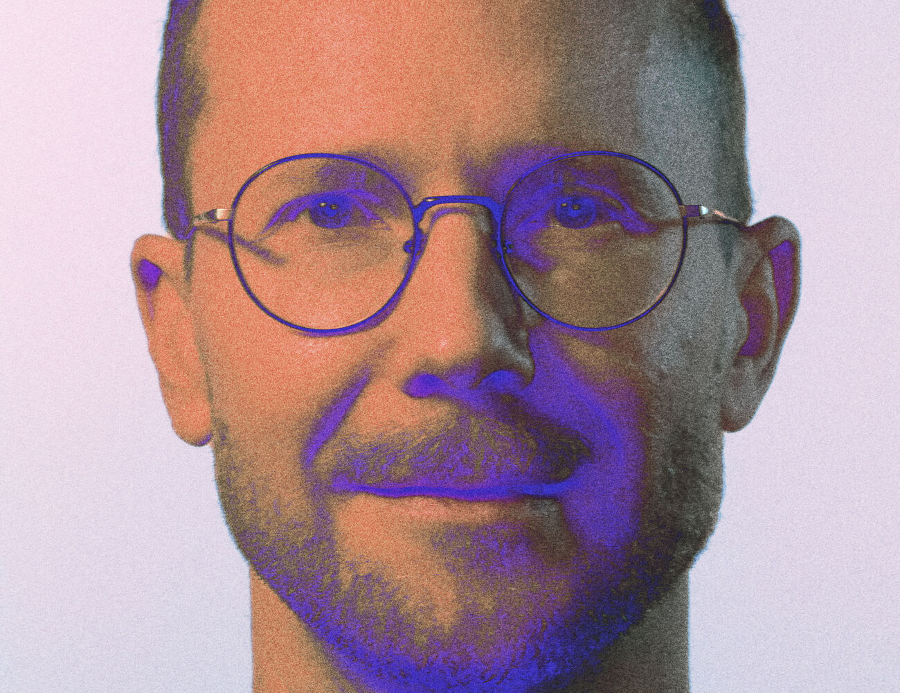 A person with short curly hair wearing a purple shirt. The background is light grey.