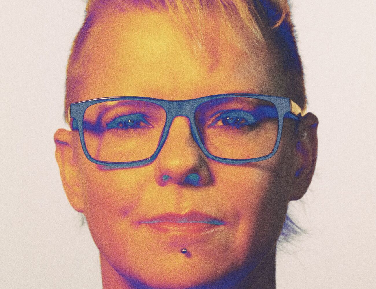 Person with short, styled hair wearing glasses and a blue shirt.