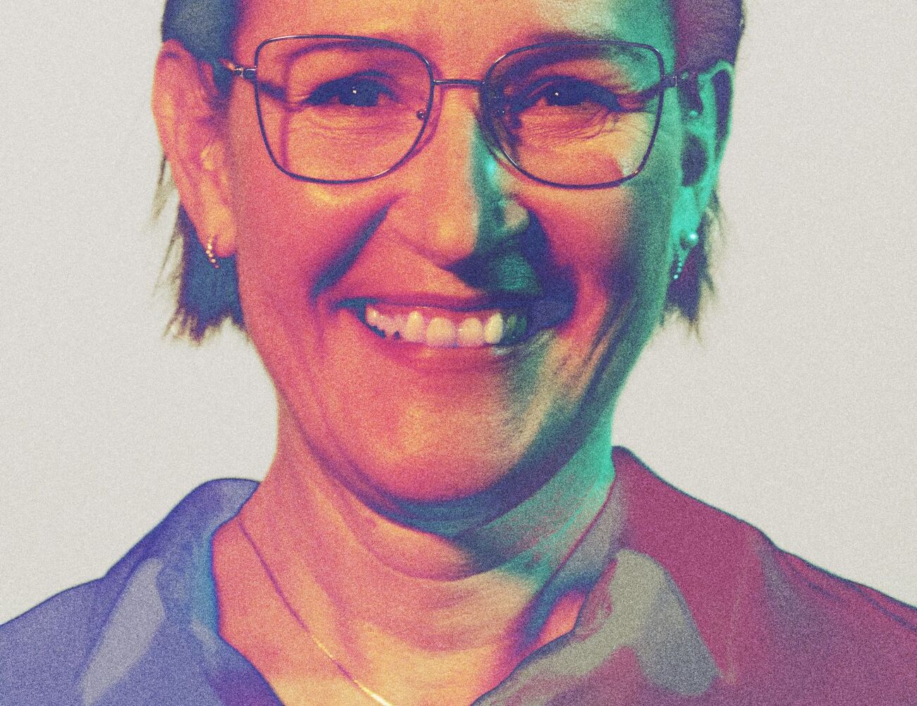A person with short hair wearing a collared shirt and a necklace with a small pendant.