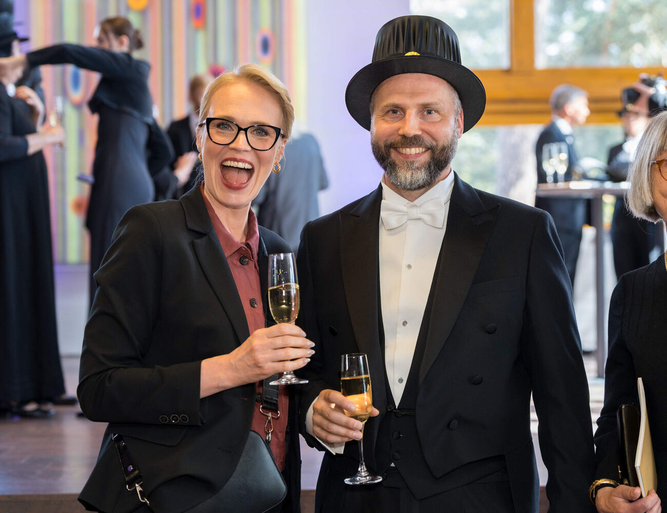 People in formal black outfits holding champagne glasses at an indoor reception with art in the background