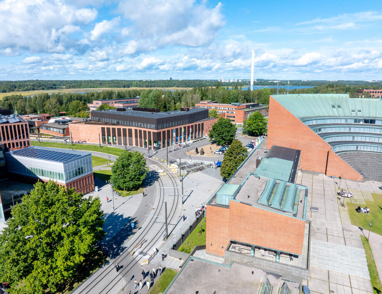Aerial view of a modern campus with red brick buildings, tram tracks and green trees on a sunny day