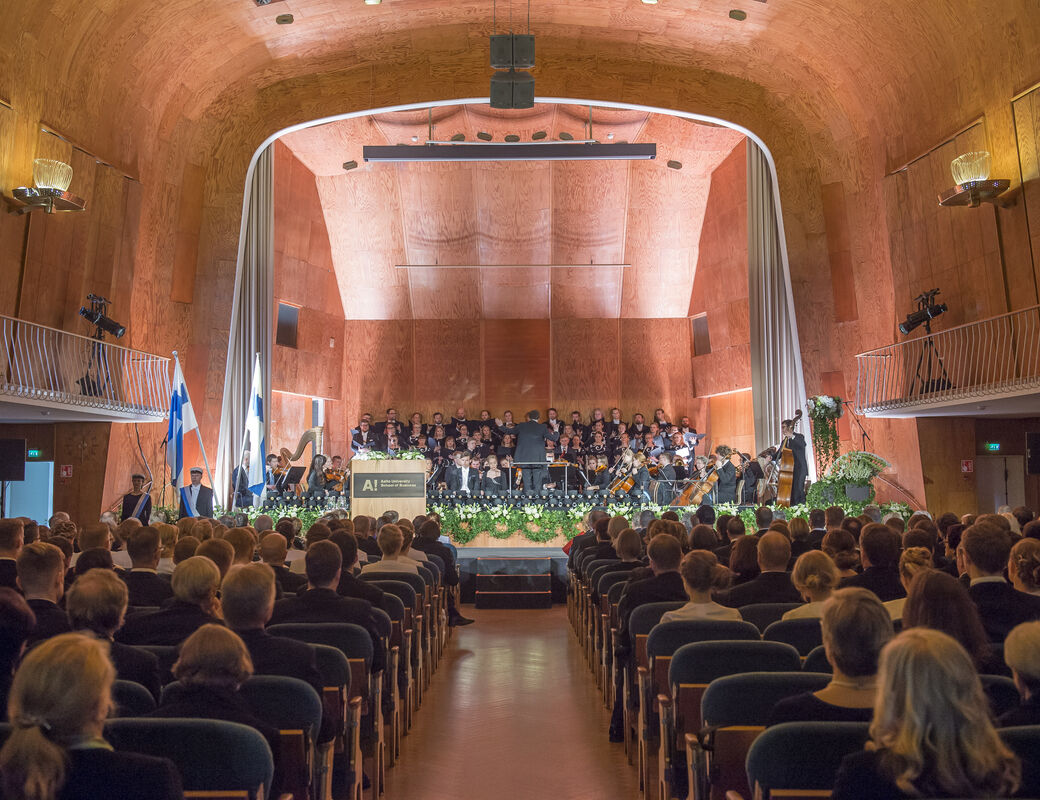Kuva Kauppakorkeakoulun promootioaktista 2016 Juhlasalissa. Kuvassa yleisöä ja sinfoniaorkesteri kukitetulla lavalla