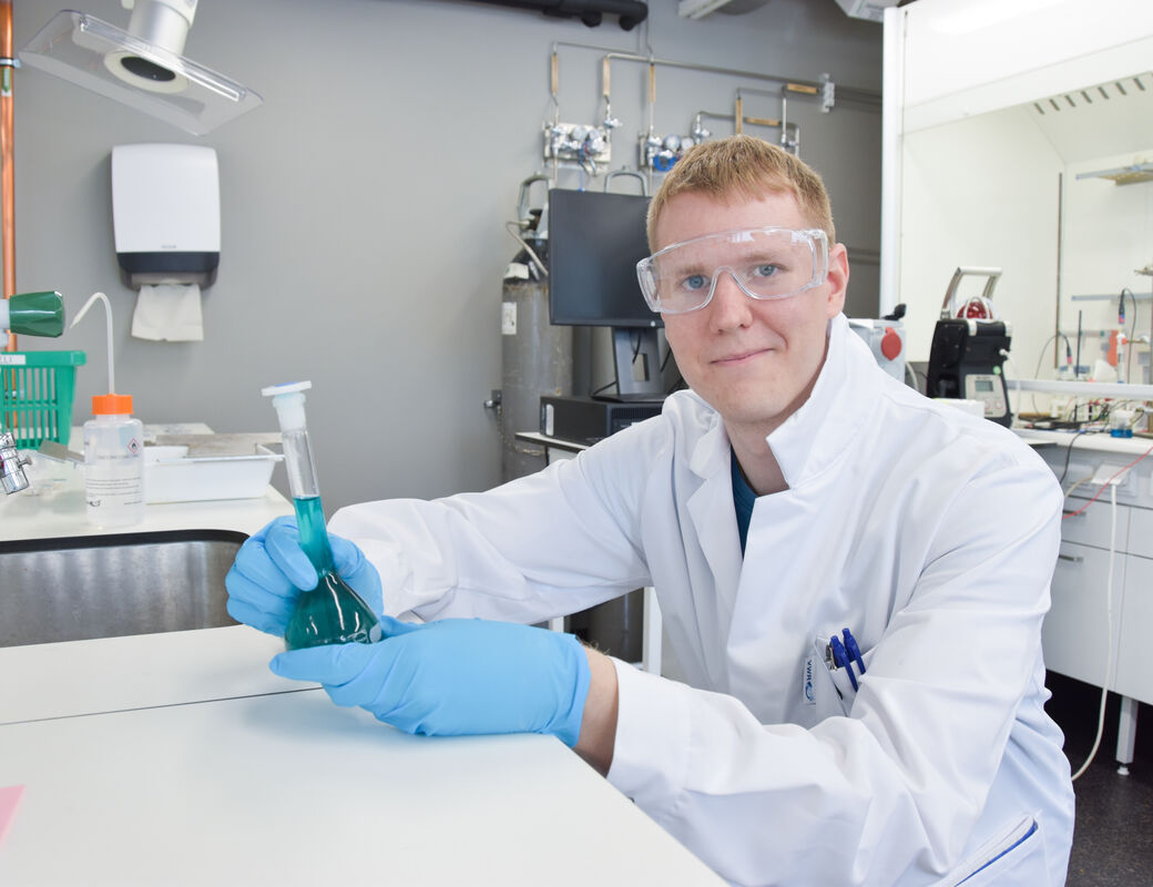 Jere in the laboratory with safety gear holding a bottle