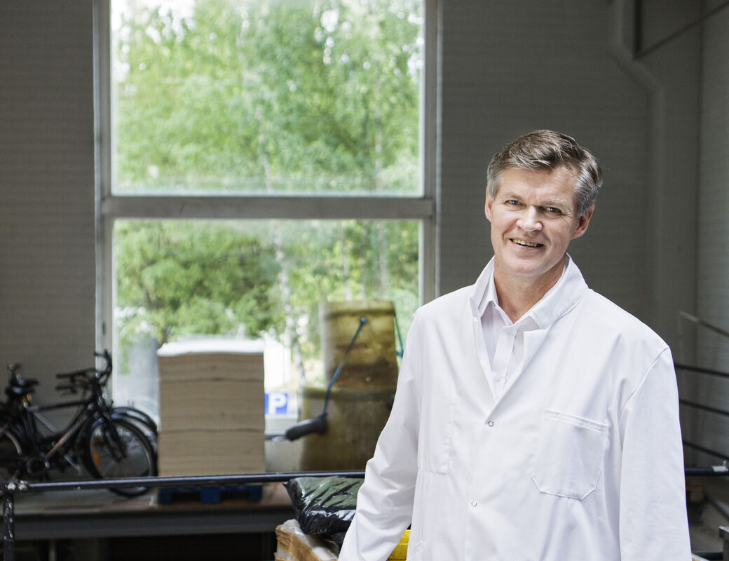 man standing in a storage in front of the window, wearing a white laboratory coat, smiling