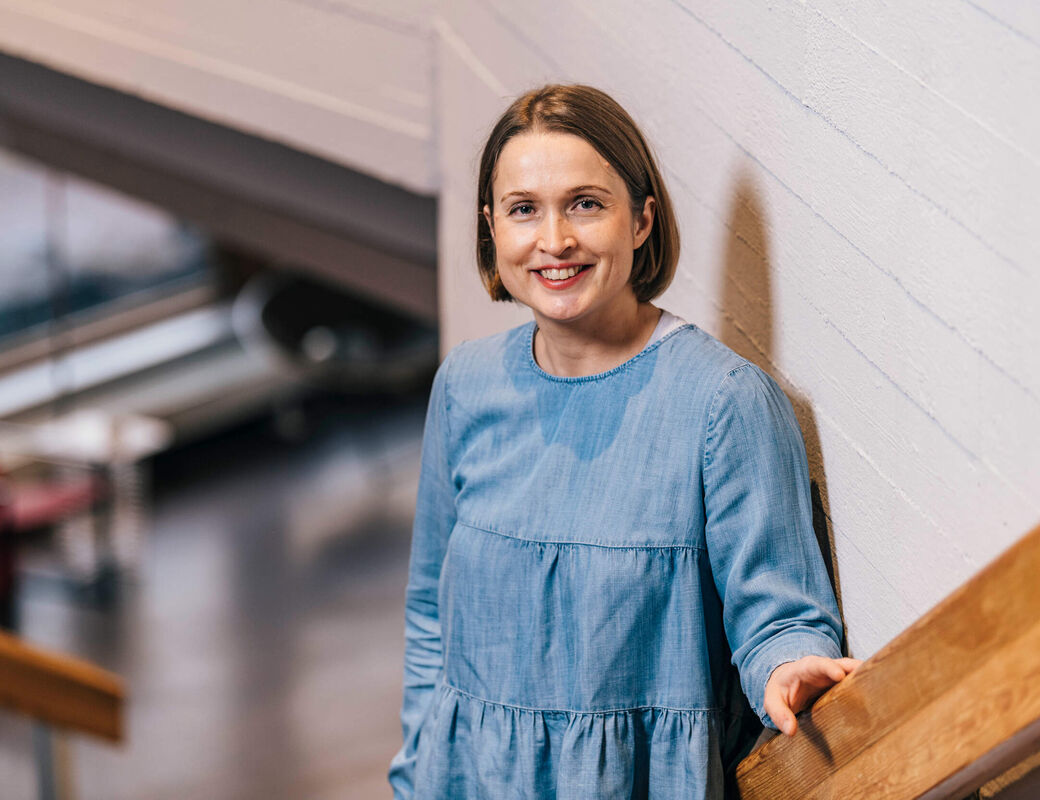 Professori Paula Jouhten nojaa kaiteeseen ja hymyilee kameralle.