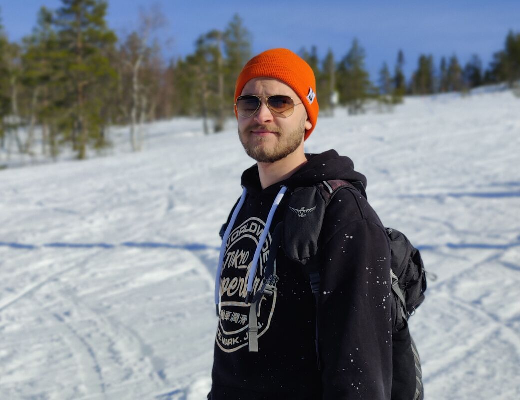 Akseli Rautakorpi kuvattuna lumisessa metsämaisemassa, aurinkolasit päässä.