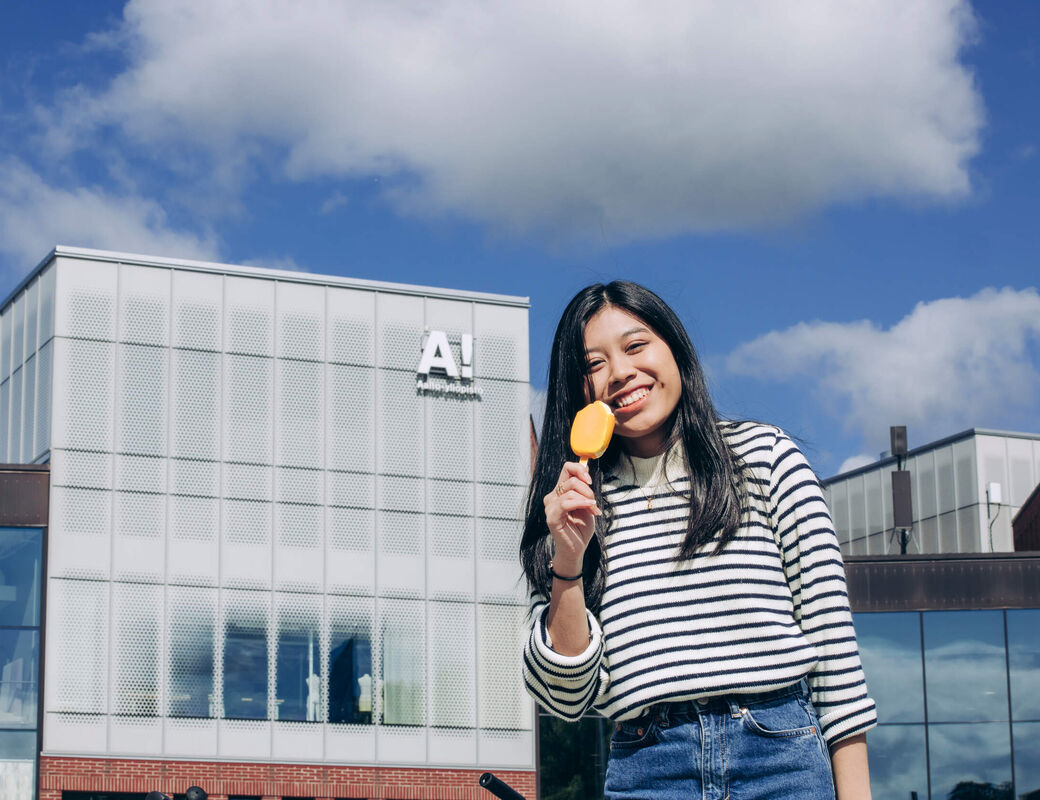 A student eating a yellow ice cream in fron of Aalto University campus.
