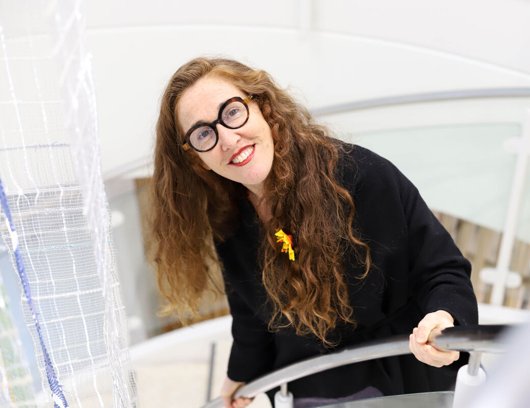 Smiling woman with glasses and long hair standing on the staircase and looking up at the camera