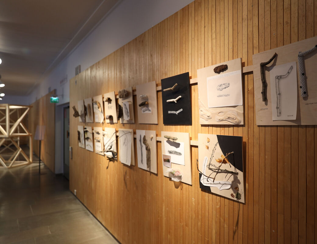 An exhibition wall with square plywood boards, each with wooden pieces and drawings thereof.